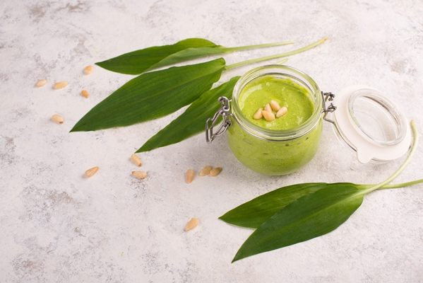 pesto made from wild garlic pine nuts and feta cheese in a glass with fresh leaves on a white - Салатный соус из черемши