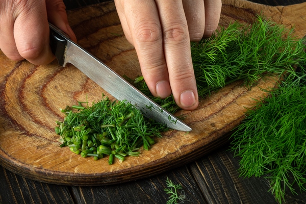 the cook cuts green dill or fennel on a cutting board with a knife for cooking vegetarian food peasant food - Пирожки с черемшой и яйцом