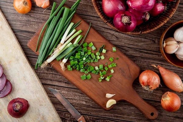 top view of cut green onion on cutting board with other onions around on wooden background - Греческий суп с одуванчиками