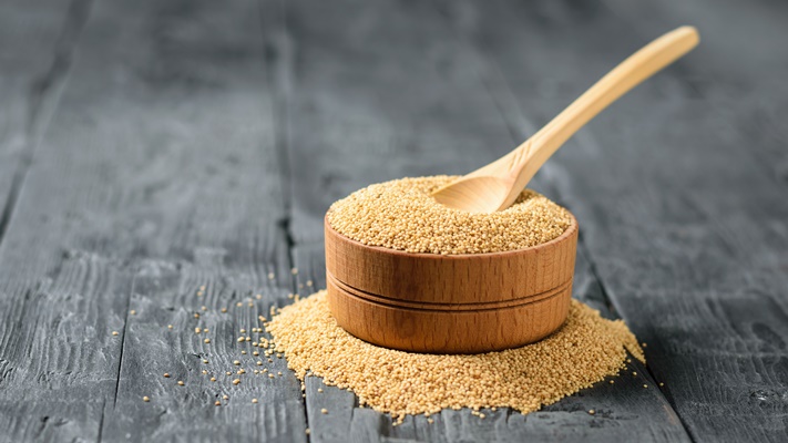 wooden bowl with amaranth seeds and a wooden spoon made of light wood on a black wooden table - Лебеда