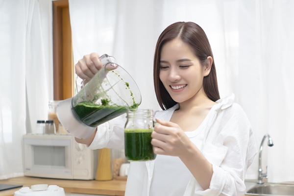 young asian woman with blender and spinach pouring to glass in minimalist kitchen at her home - Хлеб с лебедой