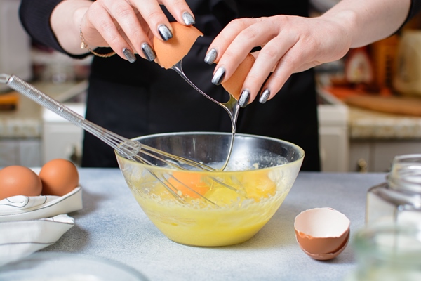 cook s hands break an egg over a glass bowl of dough - Капкейки "Красный бархат"