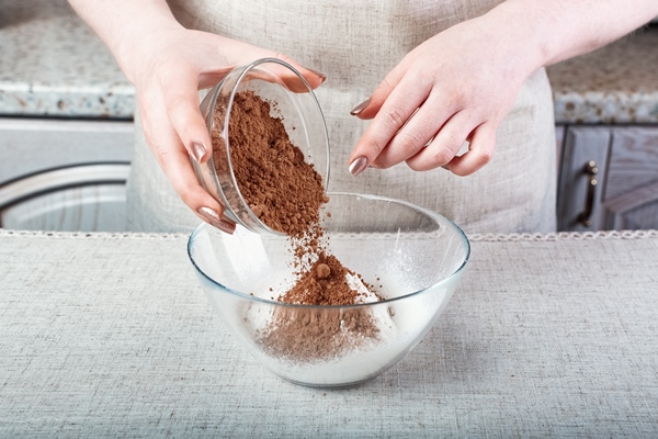 hands pouring cocoa powder into a glass bowl with flour - Капкейки "Красный бархат"