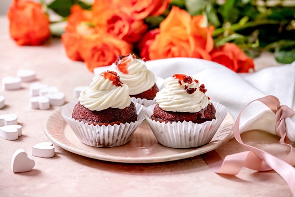 homemade red velvet cupcakes with whipped cream on pink ceramic plate white napkin with ribbon roses flowers wooden hearts over pink texture wall - Капкейки "Красный бархат"