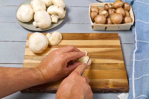 man hands cuttind fresh champignon mushrooms white and brown champignon on grey wooden table sliced champignons - Постные ленивые голубцы с грибами и рисом