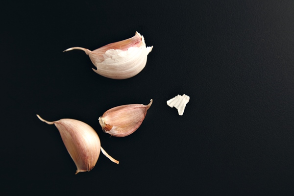 three garlic cloves and some dry peel on a smooth black background - Солёный арбуз