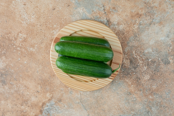 a wooden plate with fresh cucumbers on marble table - Острый фруктовый салат