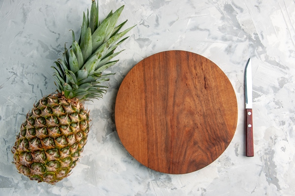 above view of whole fresh golden pineapple and cutting board knife on table on marble surface - Острый фруктовый салат