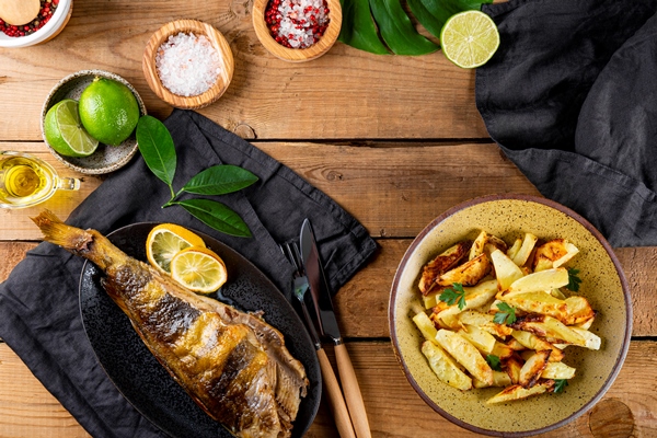 baked sea bass or lingcod fish with potatoes on the wooden table - Рыба, запечённая с яблоками и лимоном