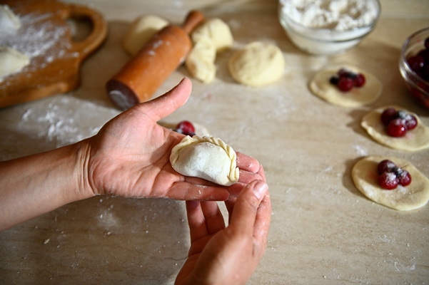 high angle view of a raw dumpling on female chef pastry hands on the background of kitchen countertop - Вареники с вишней