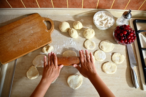 high angle view of female chef hands rolling the dough with a rolling pin on the kitchen counter to make round dumpling molds process of cooking dumplings step by step close up food background - Вареники с вишней