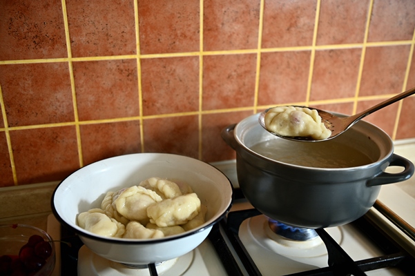 the pastry chef takes out cooked dumplings from boiling water into a colander process of cooking dumplings step by step close up food background - Вареники с вишней