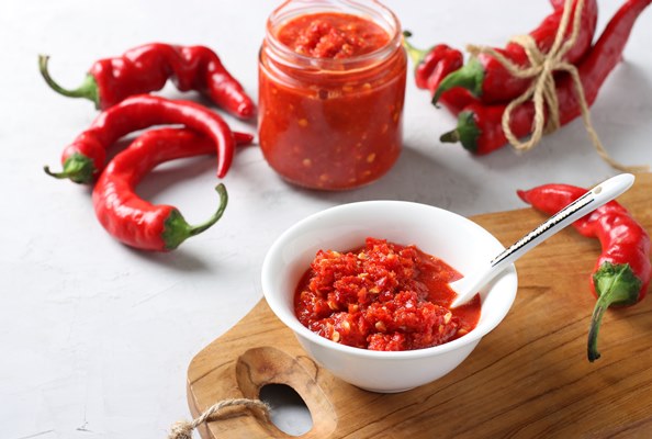 traditional sauce adjika with hot chili pepper paste harissa in bowl on wooden board closeup - Острая закуска из кабачков "Тёщин язык"