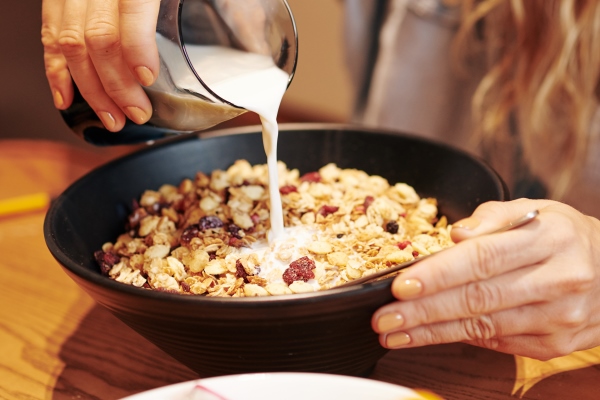 close up image of young woman adding plant milk in bowl of her morning muesli - Соевое молоко