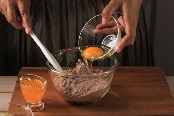 preparation mixing melted chocolate and cocoa powder in bowl to make dough for delicious brownie cake on rustic wooden table with whisk add egg yolk to the bowl - Шоколадно-миндальный брауни