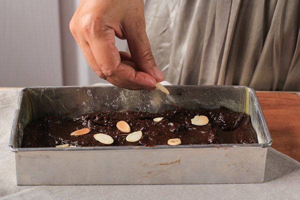 put almond above brownies mixture woman hand pour sliced almond baking process in the kitchen 1 - Шоколадно-миндальный брауни