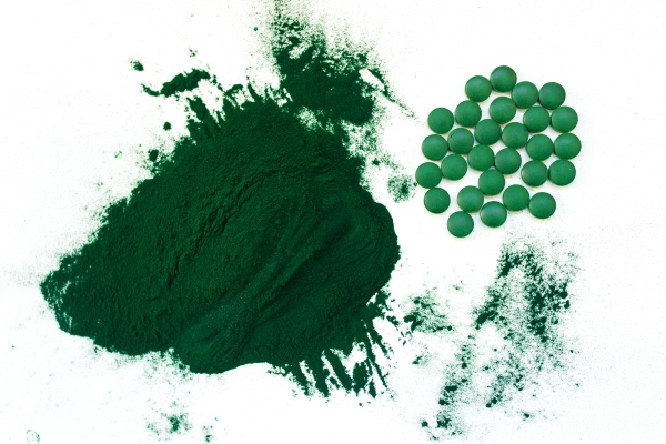 green hawaiian spirulina in tablespoons pills and powder on light white background - Съедобные водоросли