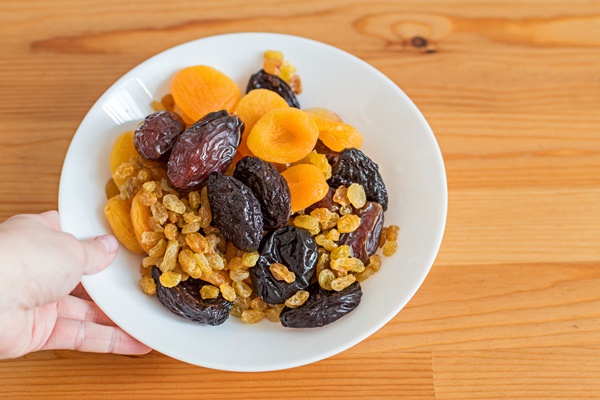 plate with dried fruits on a wooden table useful food dates dried apricots prunes raisins - Плов с сухофруктами и каштанами