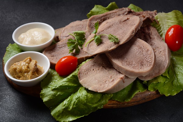 sliced beef tongue slices on a platter with lettuce leaves cherry tomatoes and dijon mustard on a wooden background - Русский столовый хрен