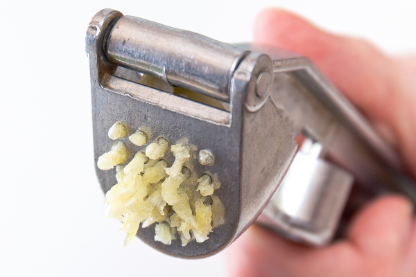 male hands hold a garlic press or garlic squeezer kitchen tool for preparing and preparing salads dishes - Домашняя кулинарная соль