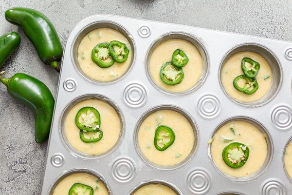 cornbread batter in muffin pans garnished with jalapeno peppers - Кукурузные маффины с халапеньо