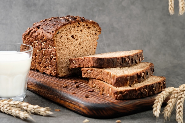homebaked bread sourdough rye bread with seeds cut into slices lies on a cutting board loaf of bread and glass of milk healthy breakfast idea selective focus close up ears of wheat on the table - Ржаной хлеб