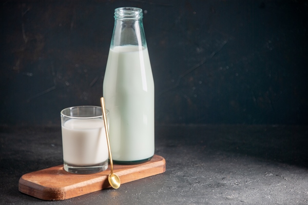 top view of delicious milk in glass and bottle golden spoon on wooden tray on the right side on dark surface - Морковное пюре (для детей до 1 года)
