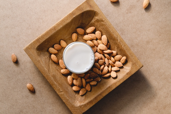 almond nuts on a wooden handmade plate and vegetarian plant milk over a kraft paper background flat lay top view - Постный смузи-боул "Щербет"