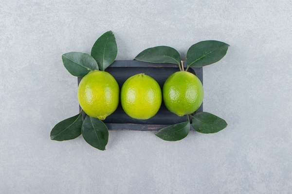 delicious lime fruits with leaves on black plate - Постный смузи-боул с огурцом, авокадо, спаржей и киви