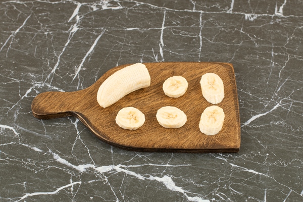 fresh banana slices on wooden board - Постный смузи-боул с финиками и орехами
