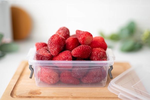 frozen ripe strawberries in a plastic container closeup - Постный смузи-боул из банана, чёрной смородины и клубники
