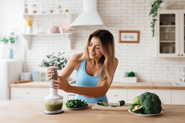excited young woman working the blender for making a smoothie of green veggies - Смузи-боул из брокколи