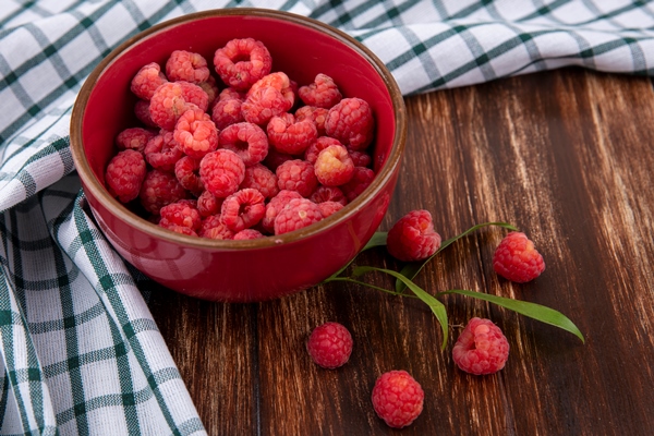 side view of raspberries in bowl on plaid cloth and leaves on wood - Постный пудинг из кешью