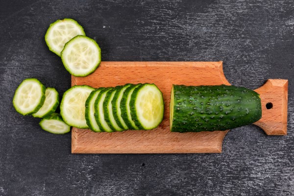 top view cucumber sliced on wooden cutting board on black stone horizontal - Смузи-боул из брокколи