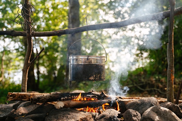 a tourist sootcovered bowler hat hangs over a smoking campfire at a forest camp in summer time - Борщ "Туристический" с грибами и тушёнкой