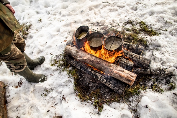 cooking in winter hike over fire in snowcovered while camping on sunny day man stands near - Организация трапезы в походе: хранение продуктов, походная кухня, утварь, меню
