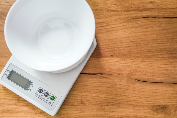 digital white kitchen scales with empty bowl on wooden table - Как перестать выбрасывать продукты и сократить расходы