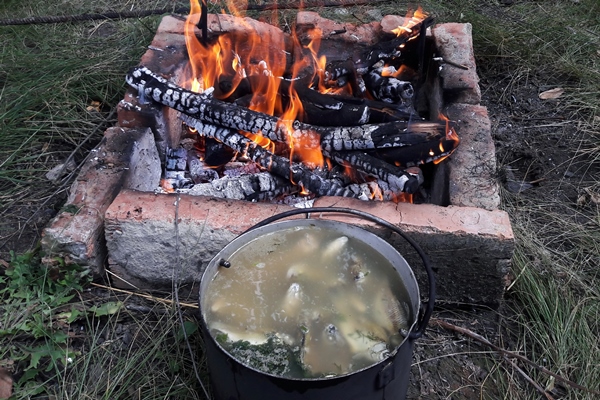fish soup cooked over a firecooked in a saucepan near a fired up grill lined with bricks - Питание в походе