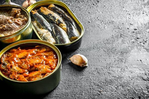 open tin cans with canned fish and meat on black rustic table - Котлеты из риса и консервов