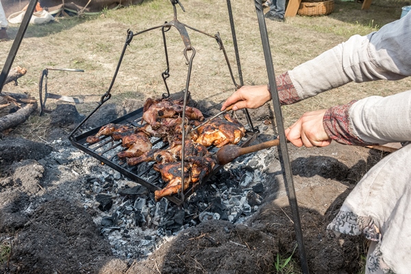 picnic at the folk art festival a man in folk clothes roasts chicken meat on a grill outdoors - Организация трапезы в походе: хранение продуктов, походная кухня, утварь, меню