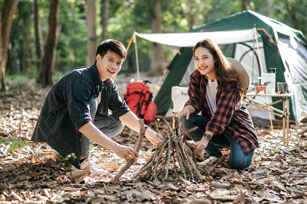 pretty camper girl preparing firewood with boyfriend to start a campfire young tourist couple helping picking branches and put them together at front of camping tent - Питание в походе