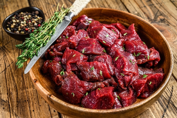 raw cut wild venison meat for a goulash in a wooden plate wooden table top view - Секреты приготовления дичи