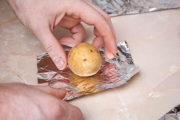 the man wraps peeled raw potatoes in foil and places them on the wire rack to bake them in the oven - Печёный на углях картофель с начинкой