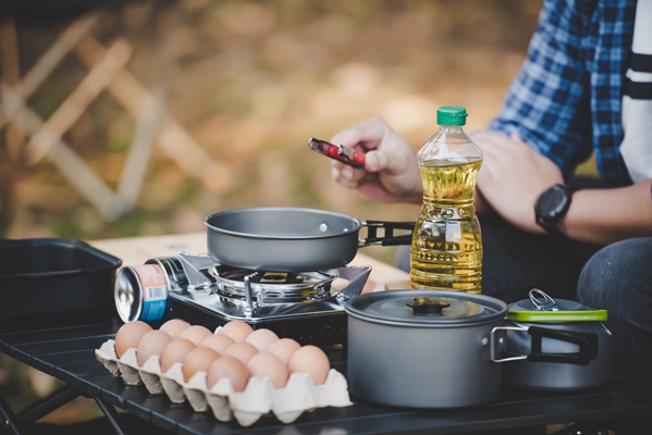 asian traveler man glasses frying a tasty fried egg in a hot pan at the campsite outdoor cooking traveling camping lifestyle concept - Яичница по-походному
