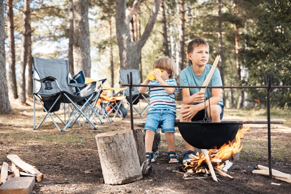 children sitting around a campfire in forest in summer family picnic outdoors camping life cooking in cauldron on fire in nature - Компот из яблок и апельсинов по-походному