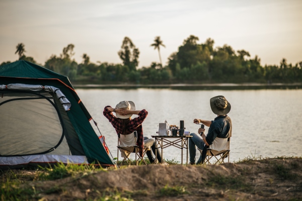 rear view of young backpacker couple sitting to relax at front of the tent near the lake with coffee set and making fresh coffee grinder while camping trip on summer vacation - Яичница по-походному