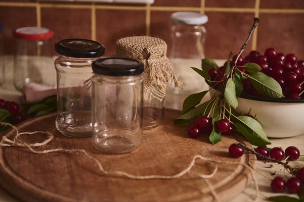 closeup of sterile jars with lids on wooden board next to a bowl with freshly picked cherries on the kitchen countertop - Вишнёвое варенье
