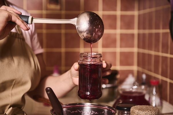 focus on ladle and glass jar in the hands of a housewife confectioner pouring freshly made cherry jam into a sterile jar in a cozy home kitchen - Вишнёвое варенье