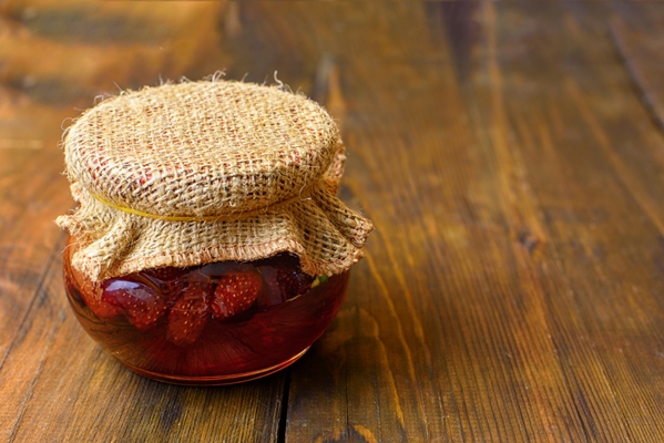 jar of strawberry jam with a lid made of burlapon dark wooden background - Клубничное варенье