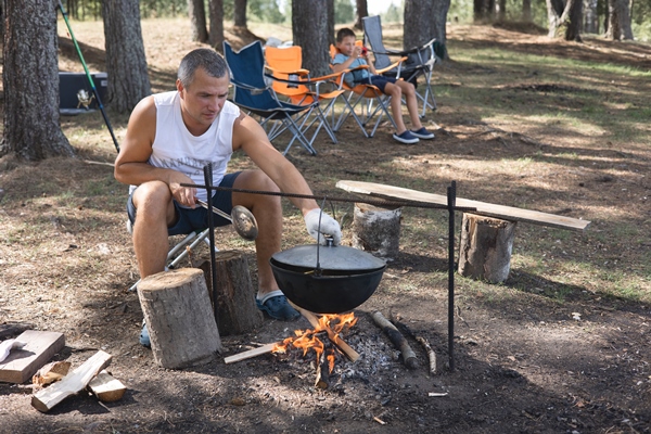 man cooking in cauldron on open fire in nature pot on bonfire on background of forest camping life local travel - Пшеничная каша в котелке на костре
